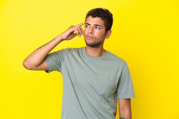 Young handsome Brazilian man isolated on yellow background making the gesture of madness putting finger on the head