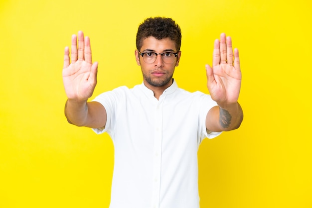 Young handsome brazilian man isolated on yellow background making stop gesture and disappointed