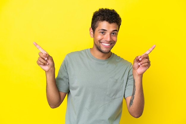 側面に指を指し、幸せな黄色の背景に分離された若いハンサムなブラジル人男性