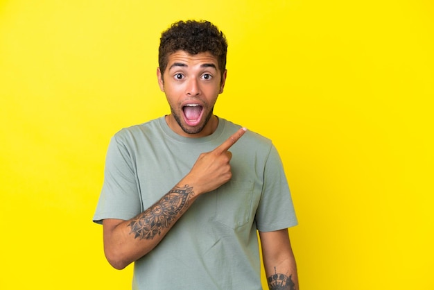 Young handsome Brazilian man isolated on yellow background surprised and pointing side