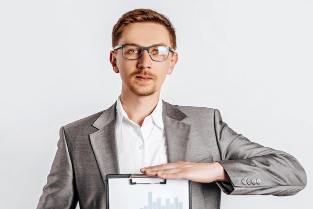 Young handsome brunette man in glasses in suit with business documents and charts on white isolated background