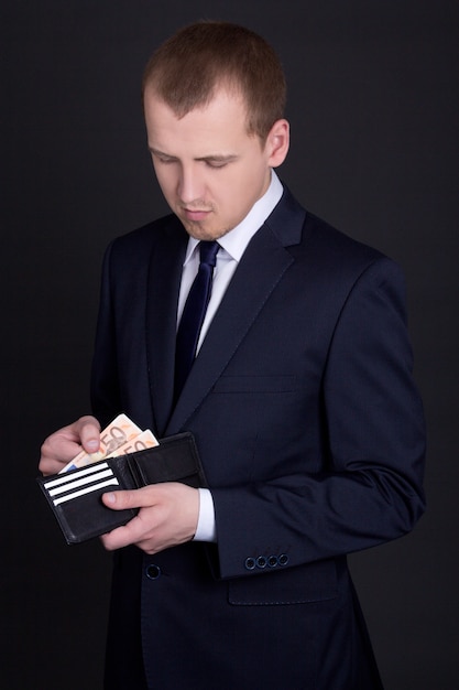 Young handsome business man holding leather purse with euro banknotes