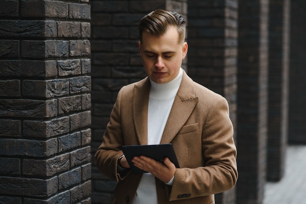 Young handsome business man using tablet computer on city street