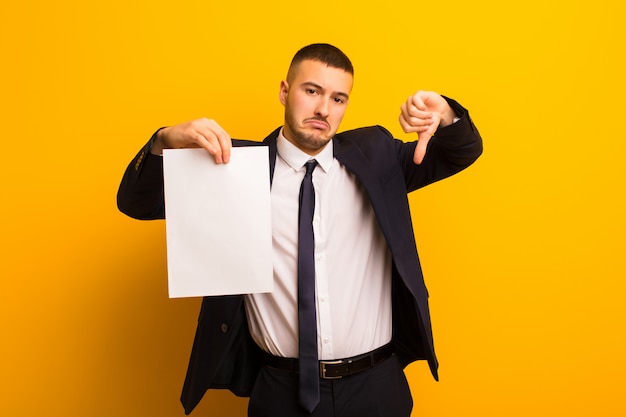 Young handsome businessman  against flat background holding an empty piece of paper