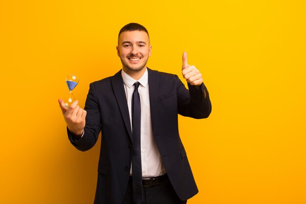 Young handsome businessman  against flat background with a sand clock timer