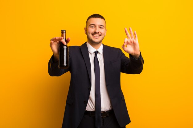 Young handsome businessman  against flat wall having a beer