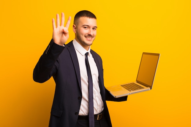 Young handsome businessman  against flat wall holding a laptop