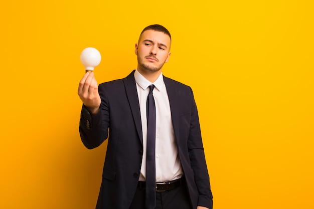 Young handsome businessman  against flat wall with a light bulb