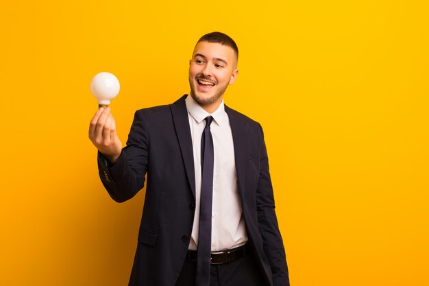 Young handsome businessman  against flat wall with a light bulb