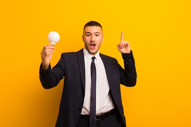 Young handsome businessman  against flat wall with a light bulb