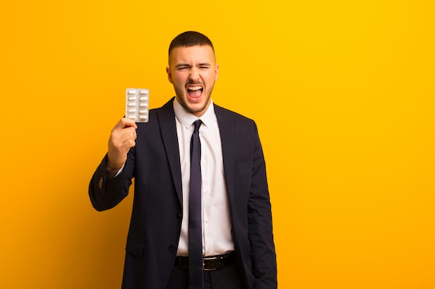 Young handsome businessman against flat wall with pills capsules