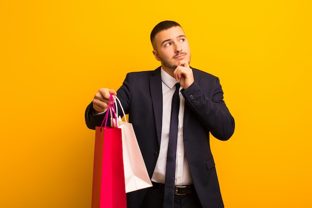 Young handsome businessman  against flat wall with shopping bags