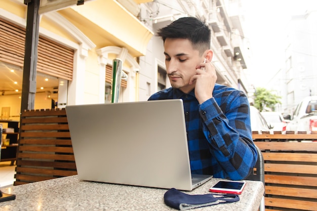 Giovane uomo d'affari bello in camicia a quadri blu usando il suo computer portatile in uno spazio pubblico.