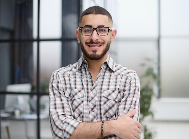 Young handsome businessman in glasses standing with crossed arms in the office