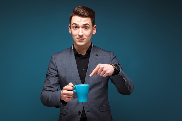 Young handsome businessman in grey jacket and black shirt hold blue cup