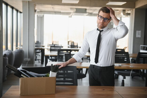 Foto giovane uomo d'affari bello in un ufficio moderno e leggero con scatola di cartone ultimo giorno di lavoro l'impiegato sconvolto viene licenziato