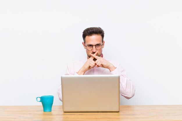 Young handsome businessman looking serious and displeased with both fingers crossed up front in rejection, asking for silence