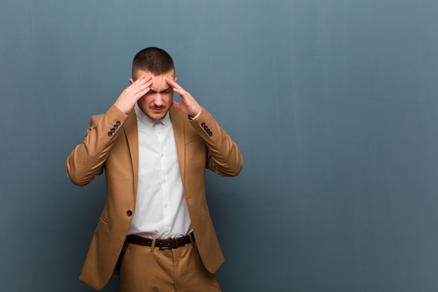 Young handsome businessman looking stressed and frustrated, working under pressure with a headache and troubled with problems against flat wall