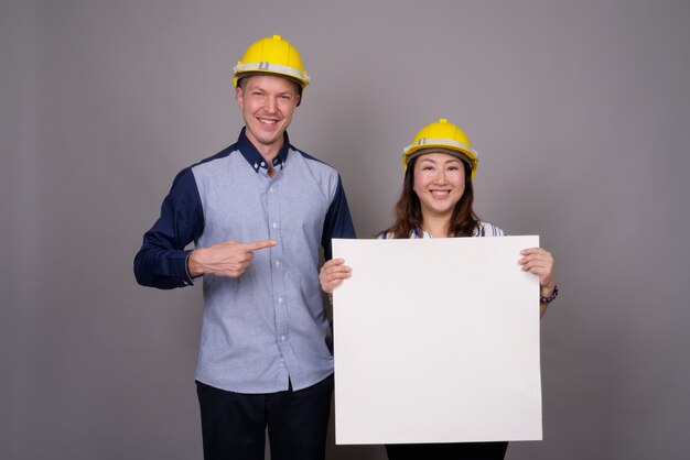 young handsome businessman and mature Asian businesswoman wearing hardhat