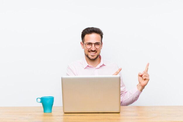 Young handsome businessman smiling happily and pointing to side and upwards with both hands showing object in copy space