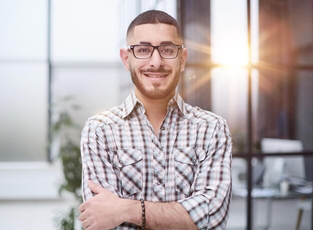 Young handsome businessman standing with arm crossed in office