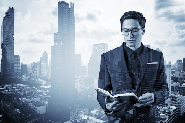 Young handsome businessman in suit and glasses thinking how to tackle the problem new career opportunities MBA assignment Bangkok on background Double exposure