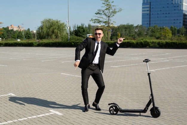 Il giovane uomo d'affari bello in un vestito guida uno scooter elettrico intorno alla città e ride
