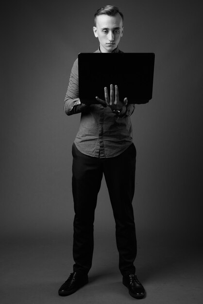 young handsome businessman using laptop against gray wall. black and white