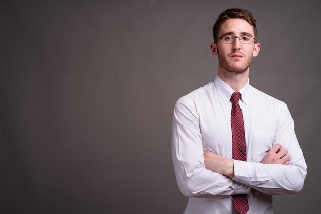 Young handsome businessman wearing eyeglasses against gray