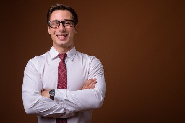 Young handsome businessman wearing eyeglasses on brown wall