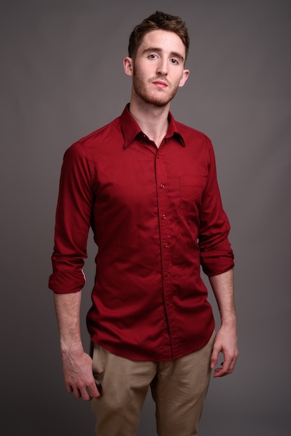 灰色に対して赤いシャツを着ている若いハンサムな実業家