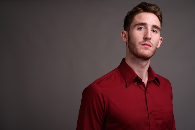 Young handsome businessman wearing red shirt against gray