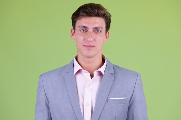  young handsome businessman wearing suit against green wall