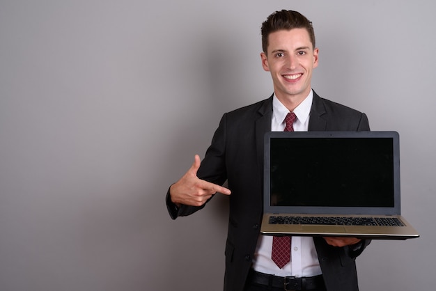 young handsome businessman wearing suit while holding laptop on gray