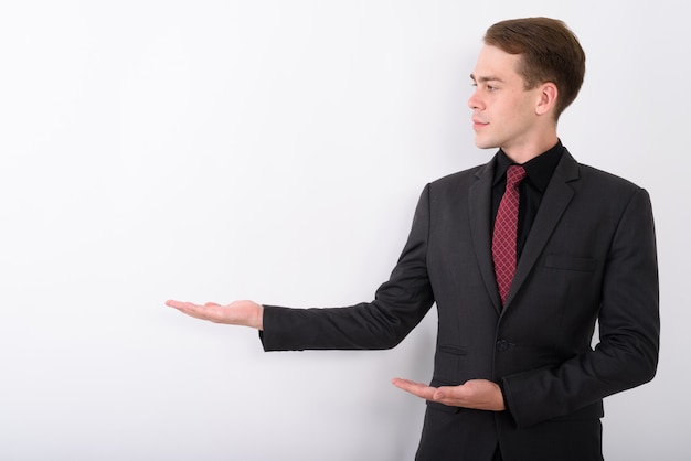 Young handsome businessman wearing suit on white wall