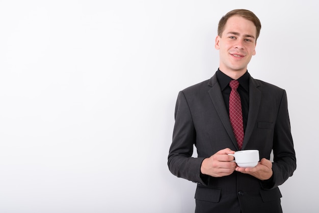 Young handsome businessman wearing suit on white wall