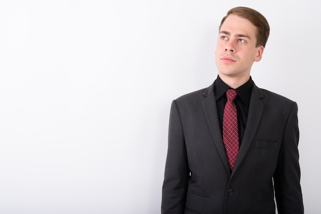 Young handsome businessman wearing suit on white wall