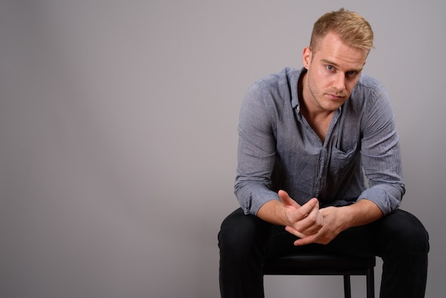 Young handsome businessman with blond hair against gray