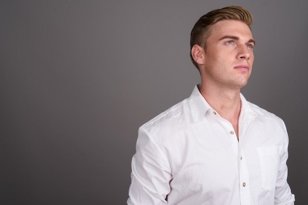 Young handsome businessman with blond hair on grey wall