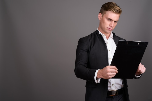 Young handsome businessman with blond hair wearing suit on grey wall