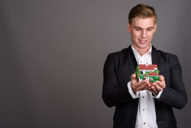 Young handsome businessman with blond hair wearing suit on grey wall