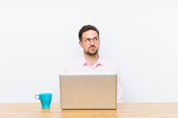 Young handsome businessman with a worried, confused, clueless expression, looking up to copy space, doubting