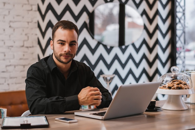 Young handsome businessman working on laptop computer in modern cafe.