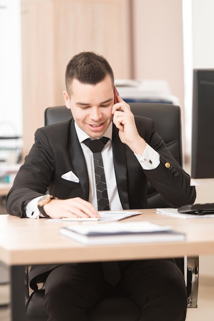 Foto giovane uomo d'affari bello che lavora con il computer alla scrivania nell'ufficio moderno che parla al telefono