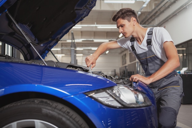 Giovane meccanico di automobile bello che ripara veicolo nel suo garage