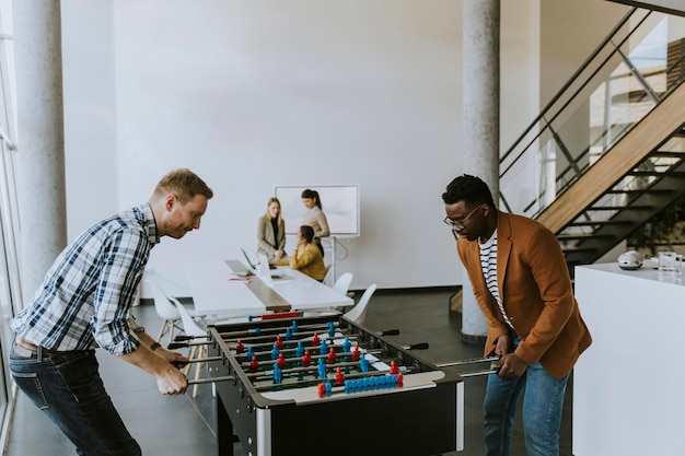 Young handsome casual multiethnic business people playing table football and relaxing at office