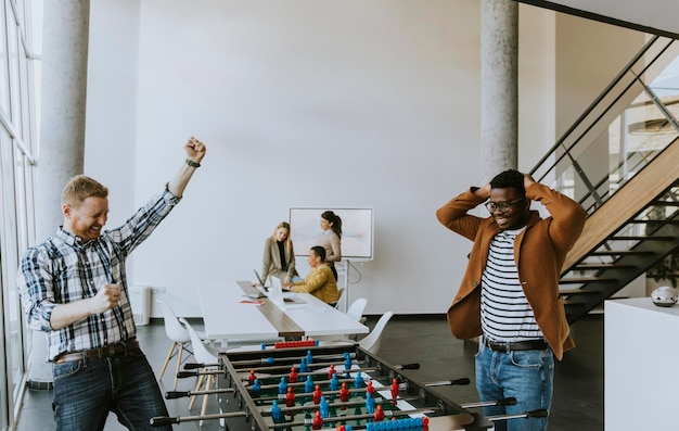 Young handsome casual multiethnic business people playing table football and relaxing at office