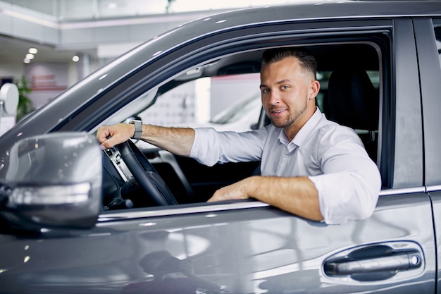 Young handsome caucasian guy sits behind the wheel of new automobile