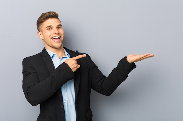 Young handsome caucasian man excited holding a copy space on palm.