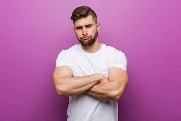 Young handsome caucasian man frowning face in displeasure, keeps arms folded.